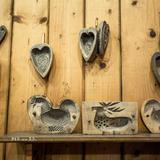 Wystawa drewnianych form do kształtowania owczych serów. Formy wiszą na drewnianej ścianie i stoją na półce.
