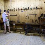 Wystawa narzędzi i wyrobów rzemieślniczych w drewnianej sali ekspozycyjnej. Ekspozycję ogląda mężczyzna z dzieckiem na rękach.