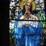 Witraż przedstawiający Maryję ubraną w niebieski szaty, z aureolą na głowie.