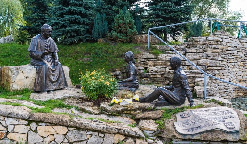 Rzeźby św. Jana Pawła II i słuchającej go pary w parku.