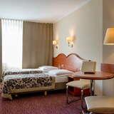 Pokój w hotelu, dwa łóżka, stolik, krzesła, szafka, lampy.