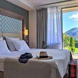 Pokój w hotelu, zasłane łóżko, otwarte drzwi na balkon z widokiem na góry.
