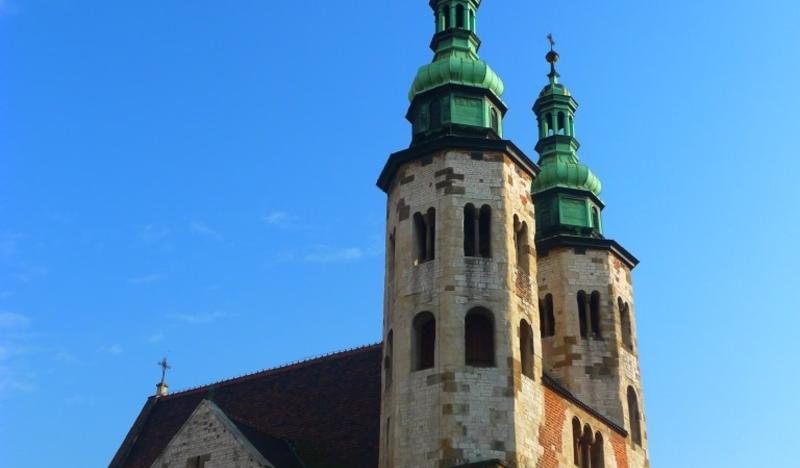 Dwie murowane wieże z cegły, z barokowymi hełmami, z boku widoczny fragment dachu.