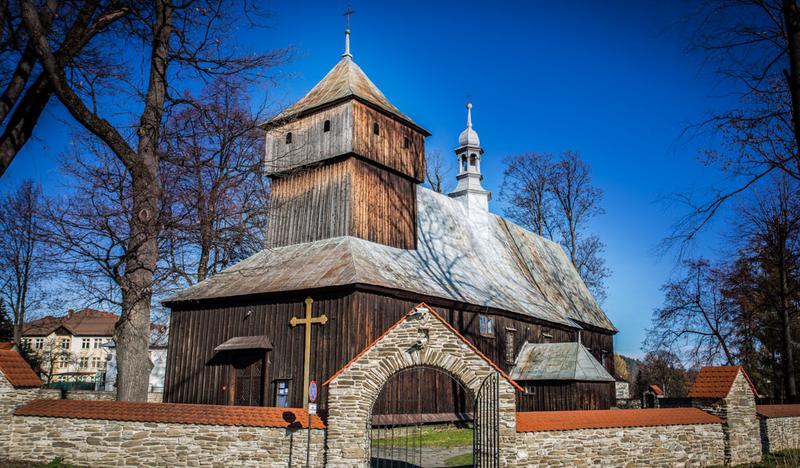 Drewniany zabytkowy kościół z blaszanym dachem, ceglany mur z wejściem dookoła kościoła