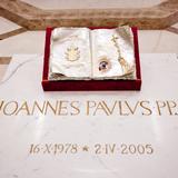Biała marmurowa płyta nagrobna  z napisem Joannes Pavlvs - PPII 16 X 1978 - 2 IV 2005. Nad nim na drewnianej podstawie otwarta księga z insygniami papieskimi.