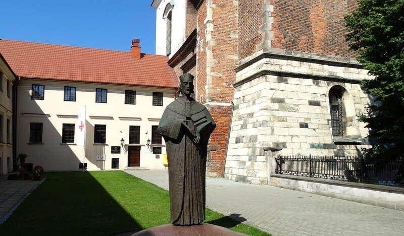 Pomnik z brązu przedstawiający mężczyznę w todze z brodą, u jego stóp jest podpis Maciej Miechowita 1457-1523.