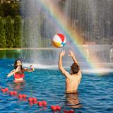 Kobieta i mężczyzna w strojach kąpielowych w basenie, podrzucający piłkę.