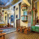 Wnętrze drewnianego kościoła z kolorowymi polichromiami, ołtarzem, ambona i ławami.