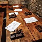 Urządzenia służące do porozumiewania się alfabetem Morse'a leżące na drewnianym stole w Muzeum Armii Krajowej w Krakowie. Za stołem znajduje się kamienna ściana.