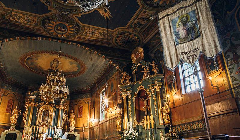 Wnętrze drewnianego kościoła, bogato polichromowane drewniane ściany, złoto-zielone barokowe ołtarze.