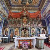 Wnętrze drewnianej cerkwi. Ołtarz główny, stół przykryty obrusem ze świecami i kwiatami w wazonie. Po prawej ambonka nakryta obrusem. Za nimi ikonostas z wieloma obrazami świętych. Ściany i sufit pokrywają kolorowe malowidła, m.in. nad ikonostasem namalowany jest baldachim. Z sufitu zwisa wieloramienny żyrandol.