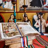 Księga liturgiczna  z wielokolorowymi zakładkami, leżąca na ołtarzu głównym, pokrytym kolorowym obrusem. Z tyłu stoją świeczniki i krzyż. Za nimi widać kolorowe obrazy świętych.