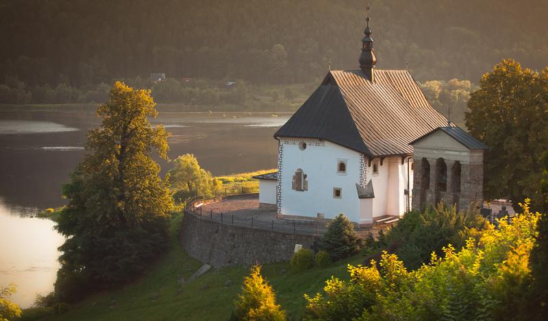 Niewielki kościół o białych ścianach stojący na wzniesieniu nad brzegiem jeziora.