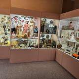 Wystawa z Muzeum Zabawek w Krynicy Zdroju w formie gabloty. Za szybą różne zabawki: lalki, pluszaki, domek dla lalek, instrumenty muzyczne i wachlarze.
