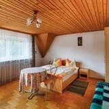 Przestronna sypialnia wykończona drewnem, z podwójnym łóżkiem, stolikiem z dwoma krzesłami oraz stolikiem nocnym. Po prawej stoi duża szafa.