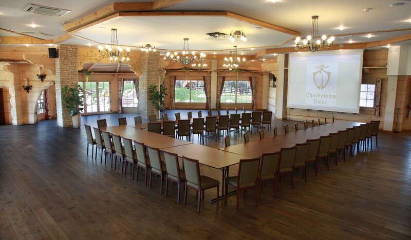 Duża sala balowo-konferencyjna z ekranem na ścianie, stołem ułożonym w podkowę i kilkudziesięcioma krzesłami dookoła.
