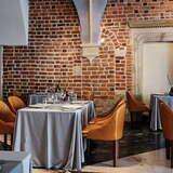 Widok na stoliki w Restauracji Trzy Rybki w Krakowie na tle ceglanej ściany. Przy stołach nakrytych szarym obrusem stoją żółte skórzane krzesła.