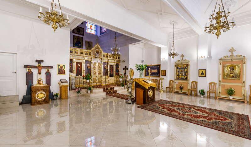 Jasne wnętrze w Cerkwii Zaśnięcia NMP w Krakowie. Na wprost znajduje się złocony ołtarz, przy ścianie są krzesła oraz ornamenty religijne.