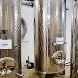 Zbliżenie na dwa metalowe zbiorniki na winogrona do produkcji wina w Winnicy Novi. Na nich widnieją nazwy gatunków Solaris oraz Johanniter.