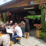 Kilkanaście osób przy stołach przed drewnianą wiatą podczas prelekcji i degustacji w Winnicy Zawadka