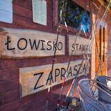 Drewniane szyldy na budynku gospodarczym na łowisku Stawki w Barcicach oraz wędki dla gości