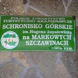 Zielona blaszana tabliczka z nazwą schroniska PTTK na Markowych Szczawinach, logo PTTK i zapisaną wysokością 1180 m n.p.m.