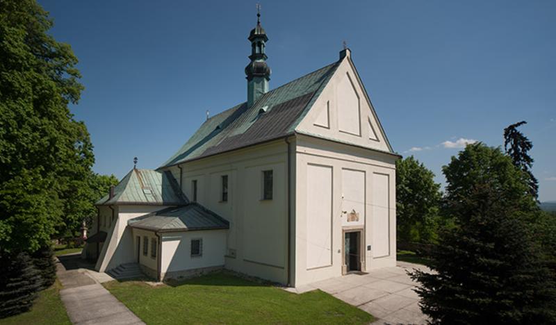 Biały, niewielki murowany kościół pokryty zielonym dachem.